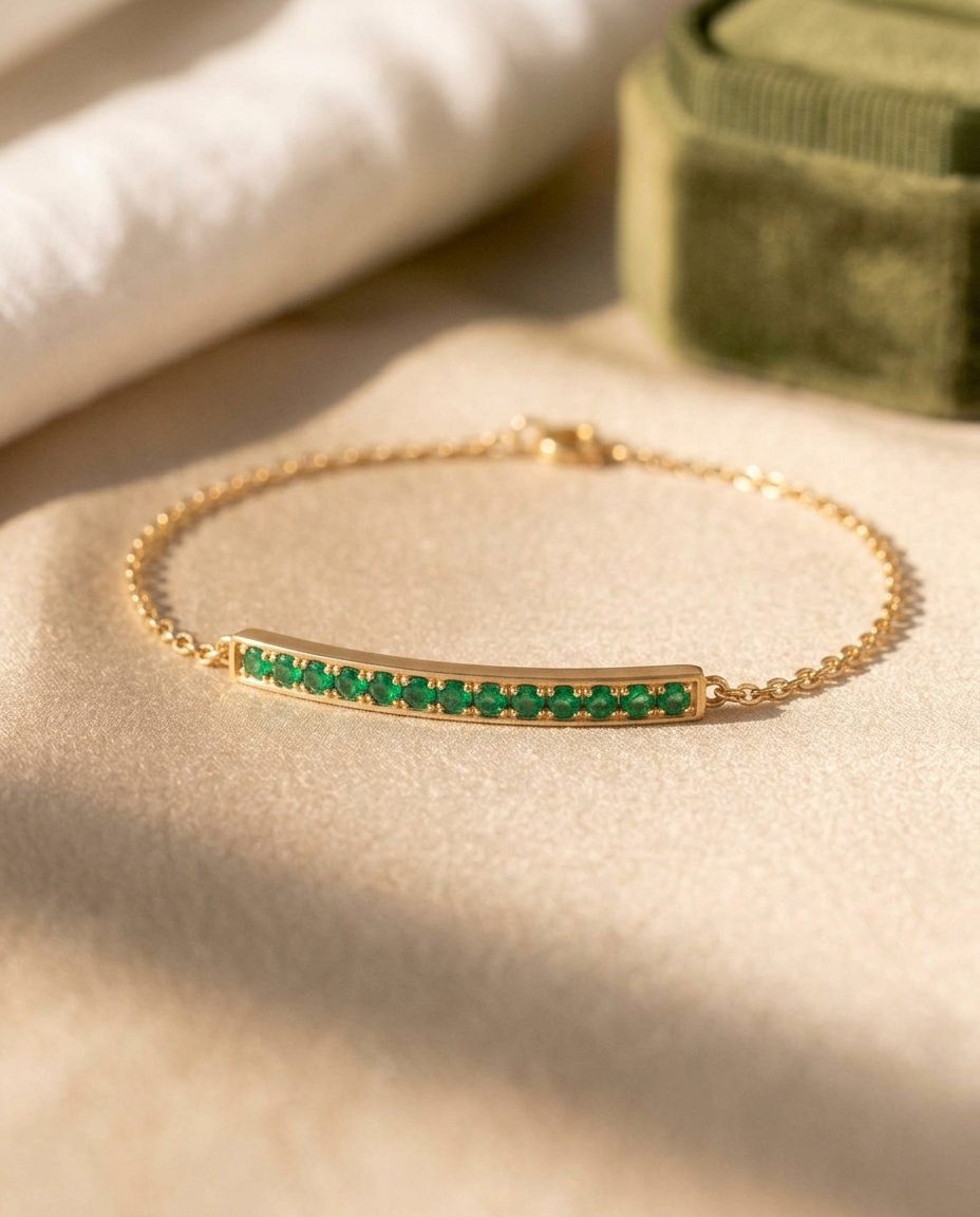 A gold chain bracelet with a flat bar set with small emeralds