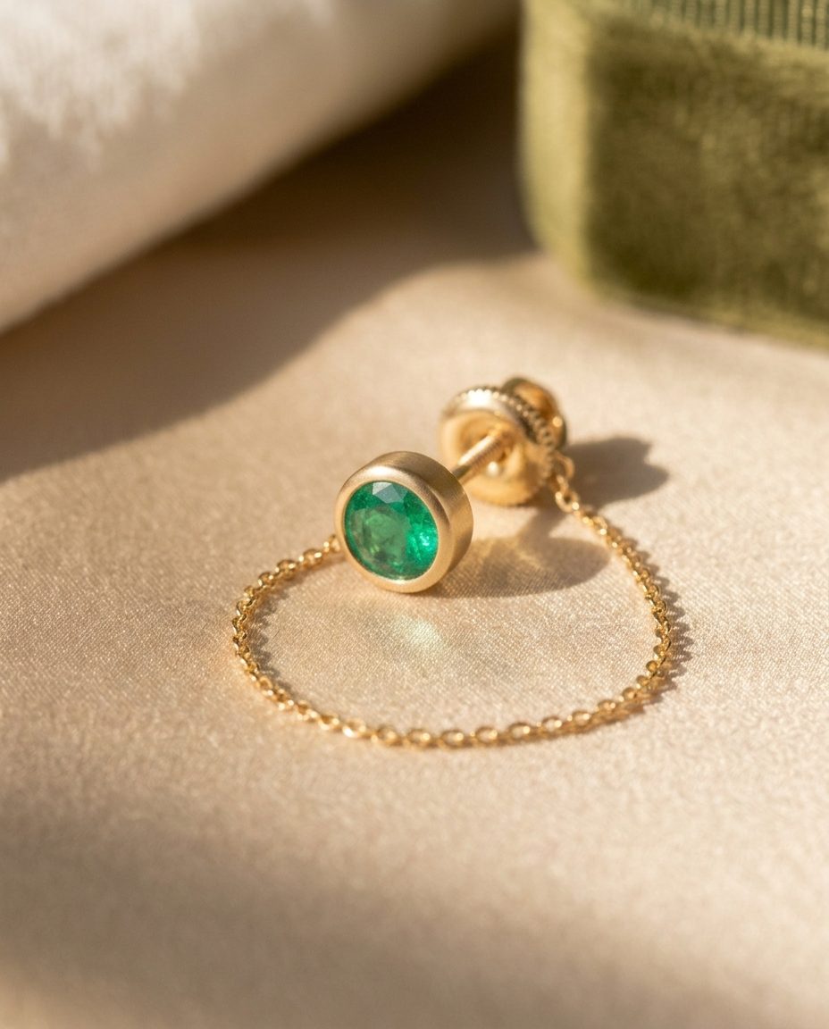 A single gold emerald stud with a fine chain draping from it