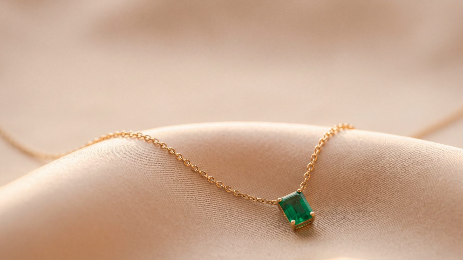 A fine gold chain with an emerald-cut pendant draped over champagne silk